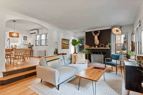 Cozy living room with a light sofa, wooden coffee table, and a deer head mounted on the wall, leading to a dining area.
