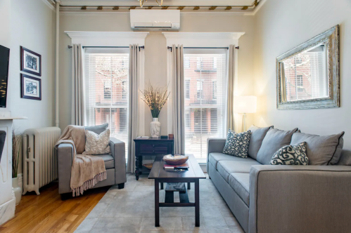 Cozy living room with gray furniture, large windows, and decorative accents, featuring a warm and inviting atmosphere.