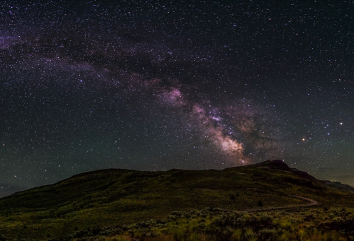 A stunning night sky filled with stars and the Milky Way over a dark, hilly landscape.