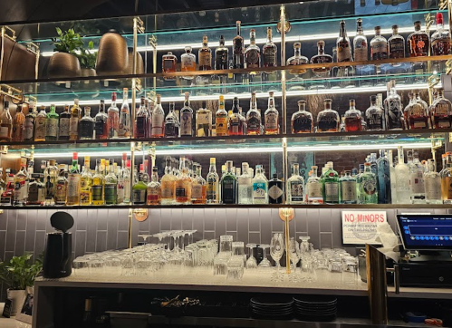 A well-stocked bar with shelves of various liquor bottles and glassware, illuminated by soft lighting.