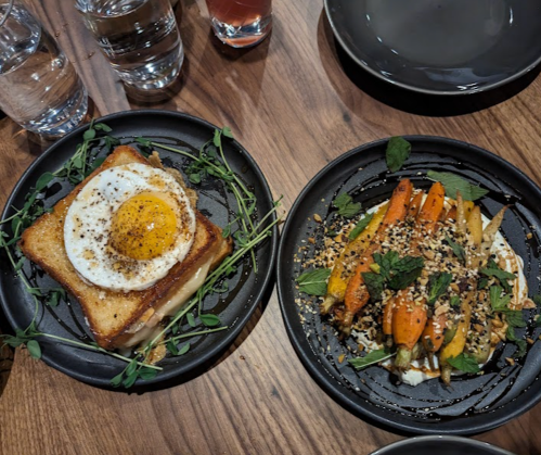 A plate with a fried egg on toast and another plate with roasted carrots topped with herbs and sesame seeds.