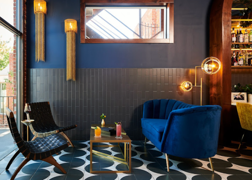 A stylish lounge area featuring a blue sofa, modern chairs, and decorative lighting against a dark wall.