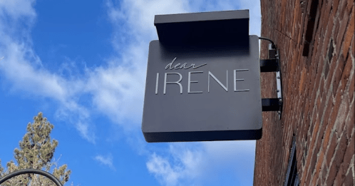Sign for "dear IRENE" on a brick building, with a clear blue sky and trees in the background.