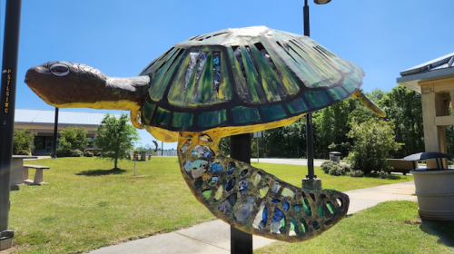 Colorful turtle sculpture with a stained glass design, mounted on a post in a sunny outdoor setting.