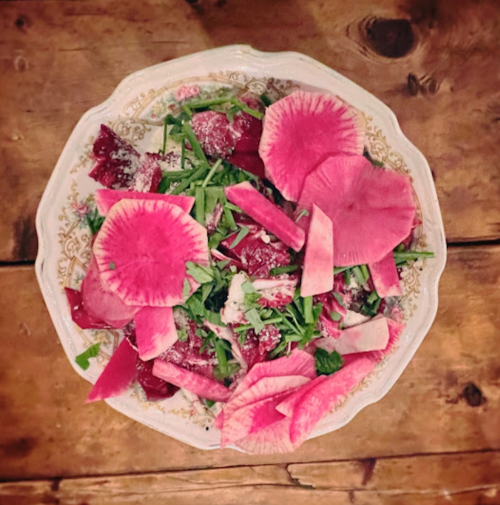 A colorful salad featuring pink radish slices, greens, and a sprinkle of cheese, served in a decorative bowl.