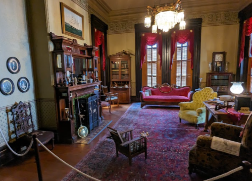 A vintage parlor with ornate furniture, a fireplace, and decorative curtains, showcasing a cozy, historical atmosphere.