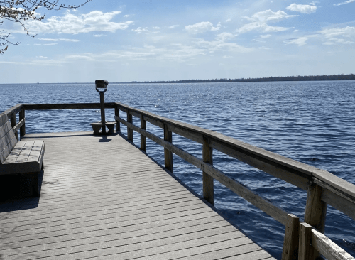 A wooden dock extends over calm water, with a scenic view of the lake and a clear blue sky.