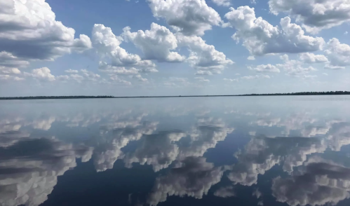 A serene lake reflecting fluffy clouds under a bright blue sky, creating a peaceful and tranquil scene.