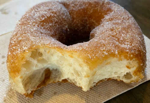A partially eaten donut coated in sugar, resting on a napkin.
