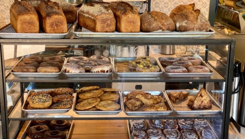 A display case filled with various baked goods, including loaves of bread and an assortment of donuts and pastries.