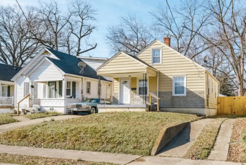 Two single-family homes on a quiet street, one with a porch and the other with a satellite dish, surrounded by trees.