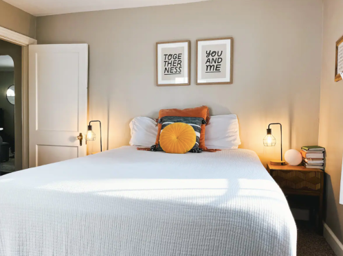 A cozy bedroom featuring a bed with decorative pillows, framed wall art, and bedside lamps in a warm, inviting atmosphere.