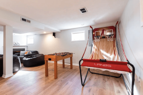 A cozy basement game room featuring a foosball table and a basketball shooting game.