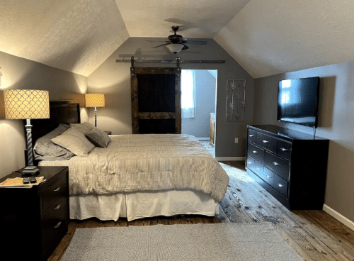 Cozy bedroom with two beds, wooden accents, a TV, and lamps, featuring a sloped ceiling and natural light.