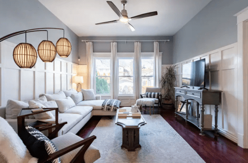 Bright living room with a sectional sofa, wooden furniture, large windows, and decorative light fixtures.