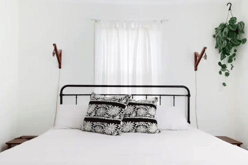 A cozy bedroom featuring a black metal bed frame, decorative pillows, and a plant hanging by the window.