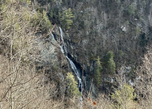 A waterfall cascading down a rocky cliff, surrounded by sparse trees and rugged terrain.