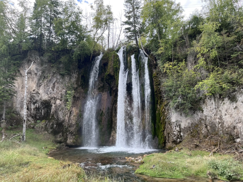 A serene waterfall cascading over rocky cliffs, surrounded by lush greenery and a clear stream below.