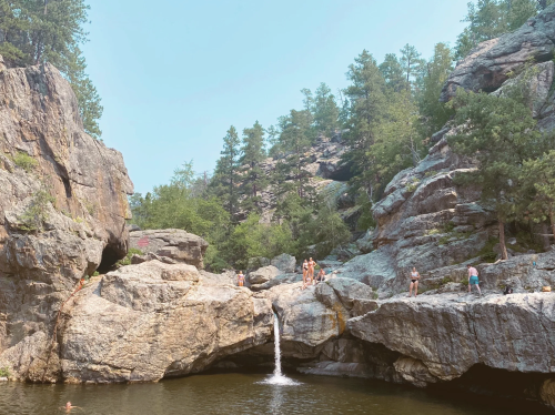 A serene natural scene featuring a small waterfall cascading into a pool, surrounded by rocky cliffs and trees.