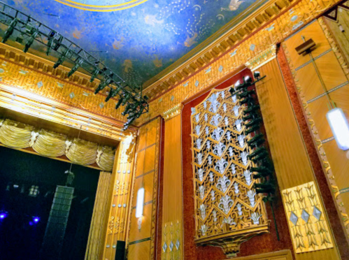 Ornate theater interior featuring a decorative ceiling and intricate wall designs, with stage lighting visible.