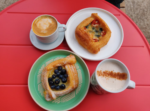 Three pastries with coffee on a red table: one with blueberries, one with vegetables, and two cups of coffee.