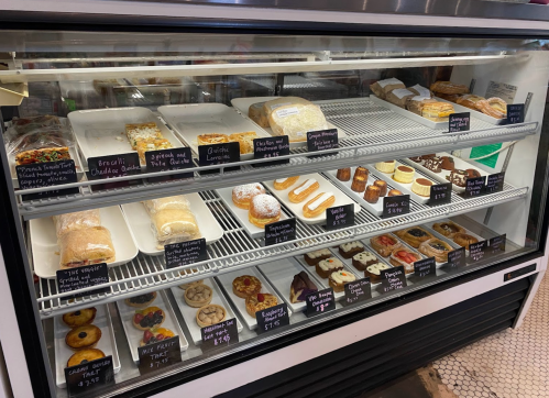 A display case filled with various baked goods, including cookies, pastries, and cakes, all labeled with prices.