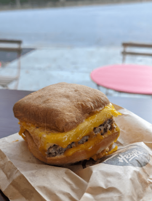 A toasted sandwich with sausage and melted cheese on a brown bun, resting on a paper wrapper.