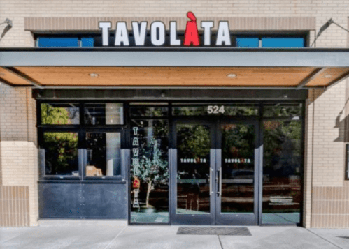 Exterior view of Tavolàta restaurant, featuring large glass doors and a modern sign above the entrance.