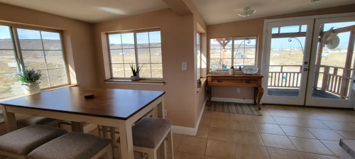 Bright interior of a room with a dining table, chairs, and large windows overlooking a scenic landscape.
