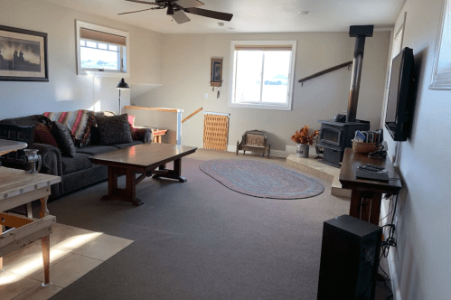 Cozy living room with a sofa, coffee table, wood stove, and decorative elements, featuring natural light and a warm atmosphere.