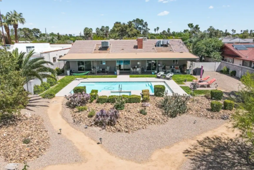 A spacious backyard with a pool, surrounded by landscaped gardens and a modern house under a clear blue sky.