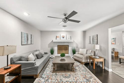 Cozy living room with a gray sofa, armchair, coffee table, and decorative art on the walls. Bright and inviting atmosphere.