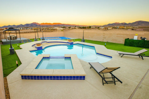 A spacious backyard with a pool, spa, and lounge chairs, set against a mountain sunset backdrop.