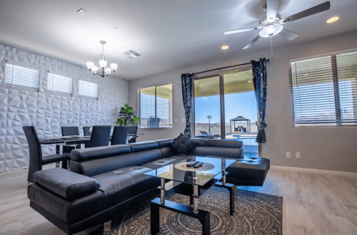 Modern living room with a black sectional sofa, glass coffee table, and large windows overlooking a patio and outdoor space.