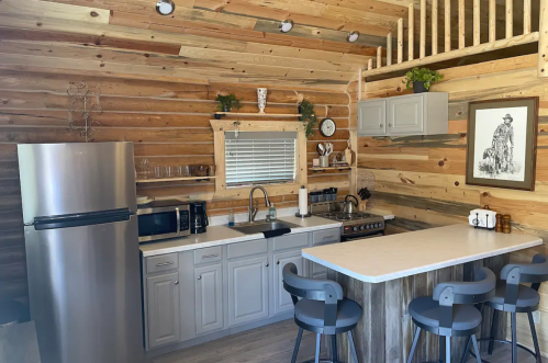 Cozy kitchen in a wooden cabin featuring a fridge, stove, sink, and bar seating with rustic decor.