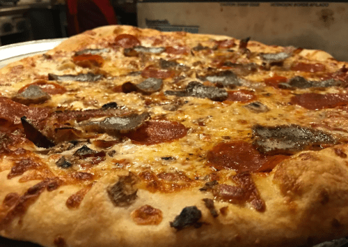 A close-up of a delicious pizza topped with pepperoni, sausage, and melted cheese, on a metal tray.