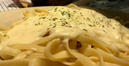 A close-up of fettuccine pasta topped with creamy cheese sauce and sprinkled with parsley.