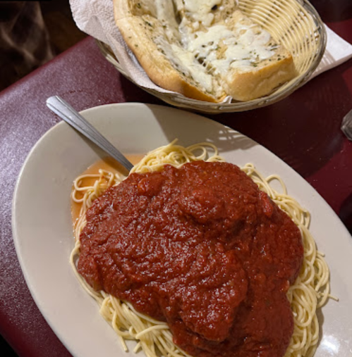 A plate of spaghetti topped with marinara sauce, alongside a basket of garlic bread.