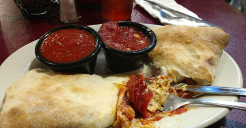 A plate with two calzones and two cups of marinara sauce, with a fork resting on the plate.