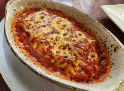 A baked pasta dish in a ceramic dish, topped with melted cheese and served in a rich tomato sauce.