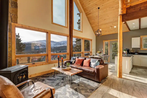 Cozy living room with large windows, mountain views, a fireplace, and modern decor in a cabin setting.