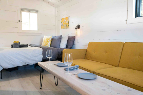 Cozy interior of a small room featuring a bed, yellow couch, and a wooden coffee table set for two.
