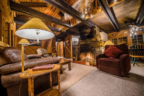 Cozy cabin interior with a stone fireplace, wooden beams, and comfortable seating, creating a warm atmosphere.