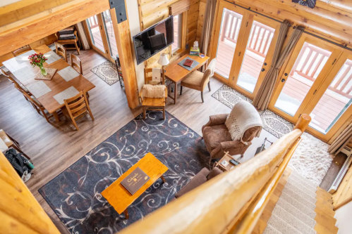 Cozy wooden interior of a cabin, featuring a living area, dining table, and large windows with a view of the outdoors.