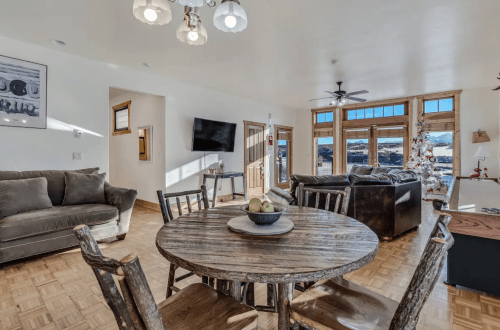 Cozy living area with a wooden dining table, comfortable sofas, and large windows showcasing a scenic view.