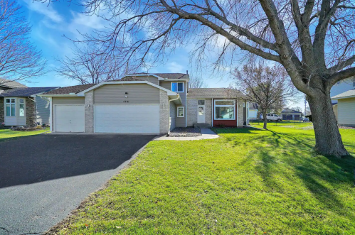 A suburban home with a driveway, green lawn, and trees under a clear blue sky.