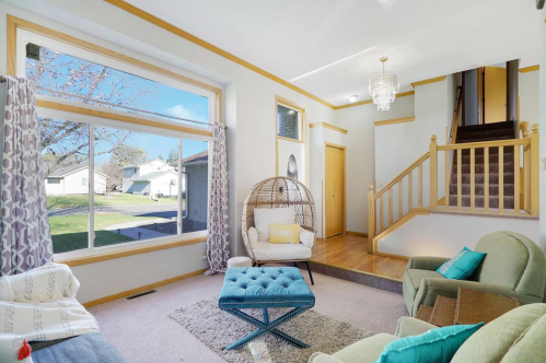 Bright living room with large window, cozy seating, and a stylish hanging chair, leading to a staircase.