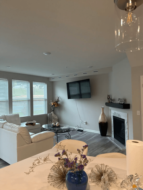 A modern living room with a white sofa, coffee table, TV on the wall, and decorative elements, featuring large windows.