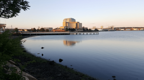 A calm waterfront scene at sunset, featuring a modern building reflecting in the water.