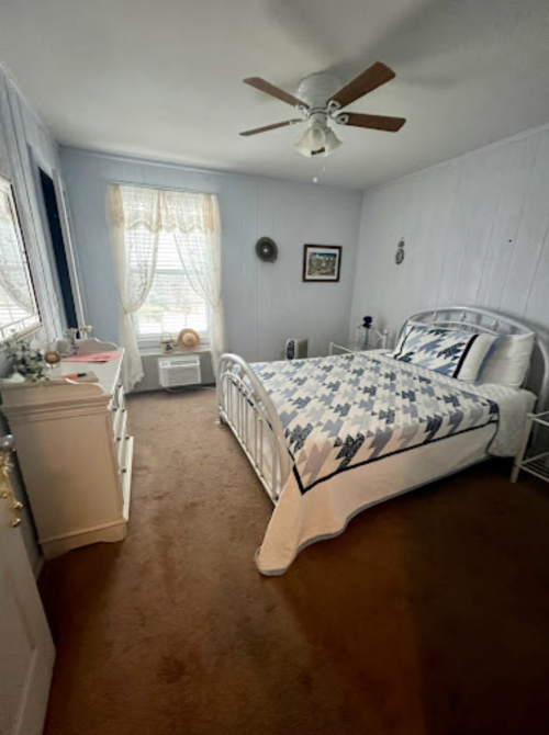 Cozy bedroom with a bed, dresser, and window, featuring light-colored walls and a quilted bedspread.